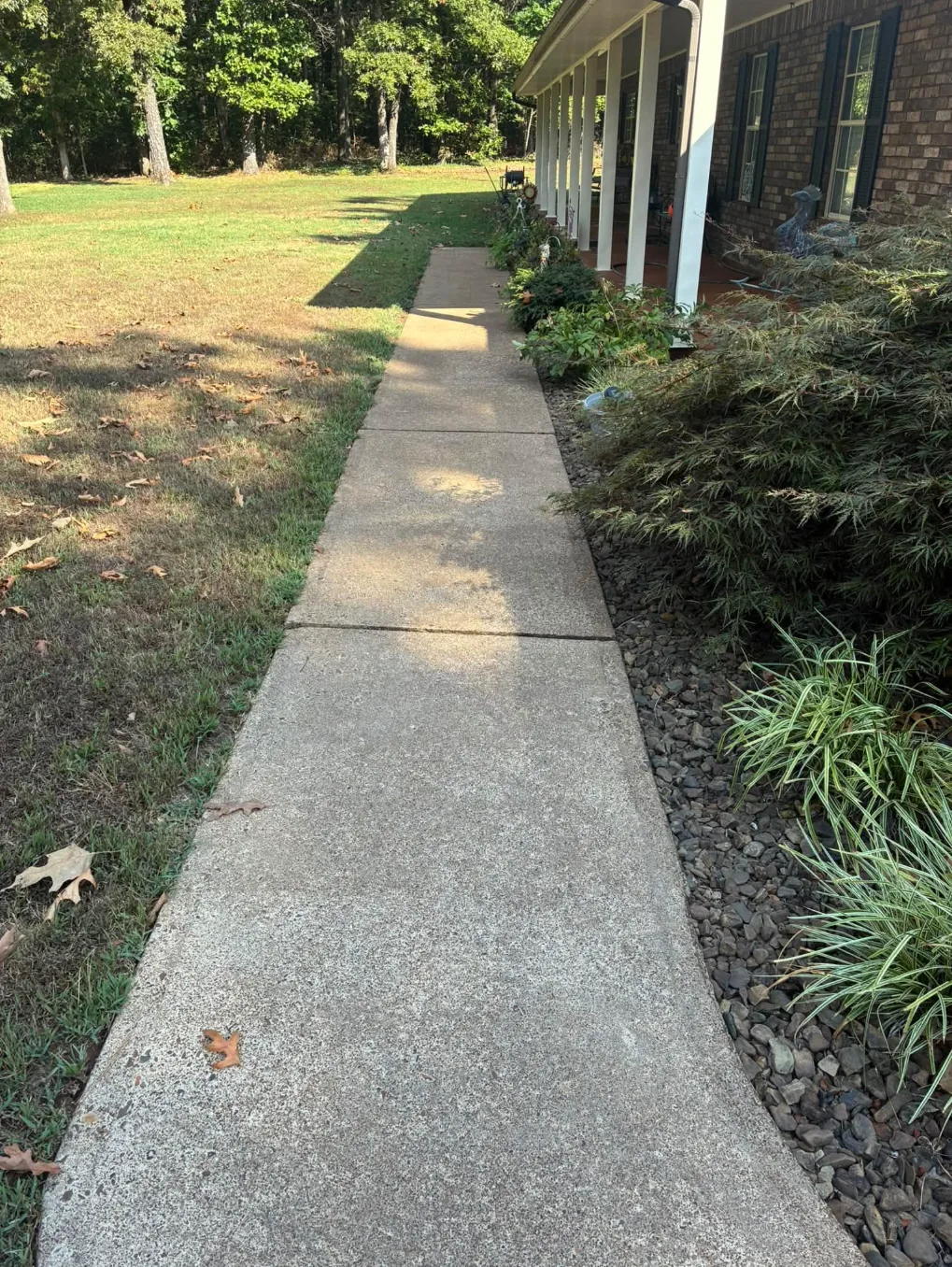 Clean concrete sidewalk running along a brick house with garden beds and rock