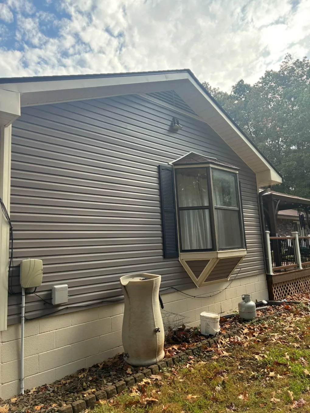 Gray vinyl siding with a dark bay window, dirty before washing