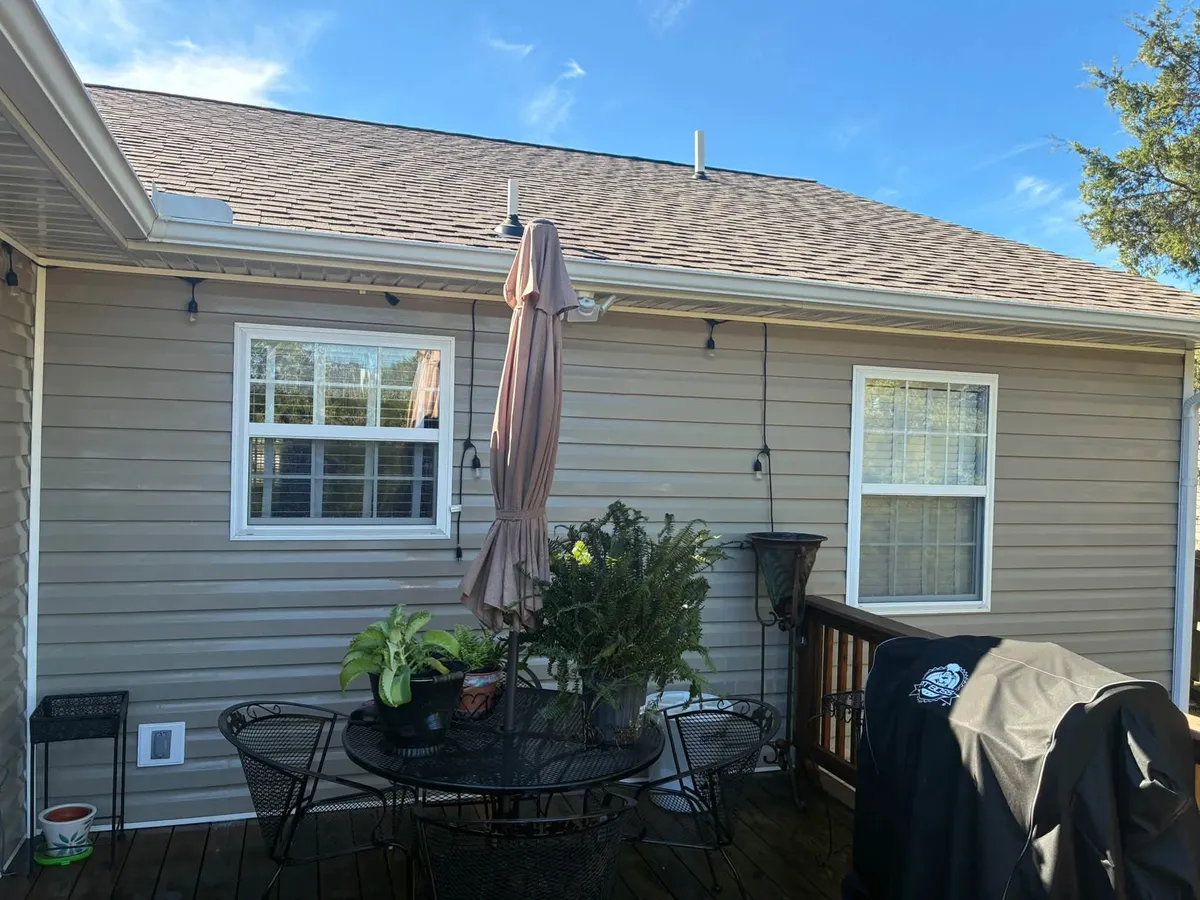 Back deck with a patio table and umbrella beside a tan sided house