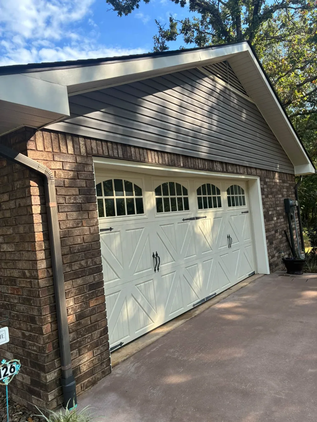 Gray vinyl siding and brick above a cream garage door, washed clean under a blue sky