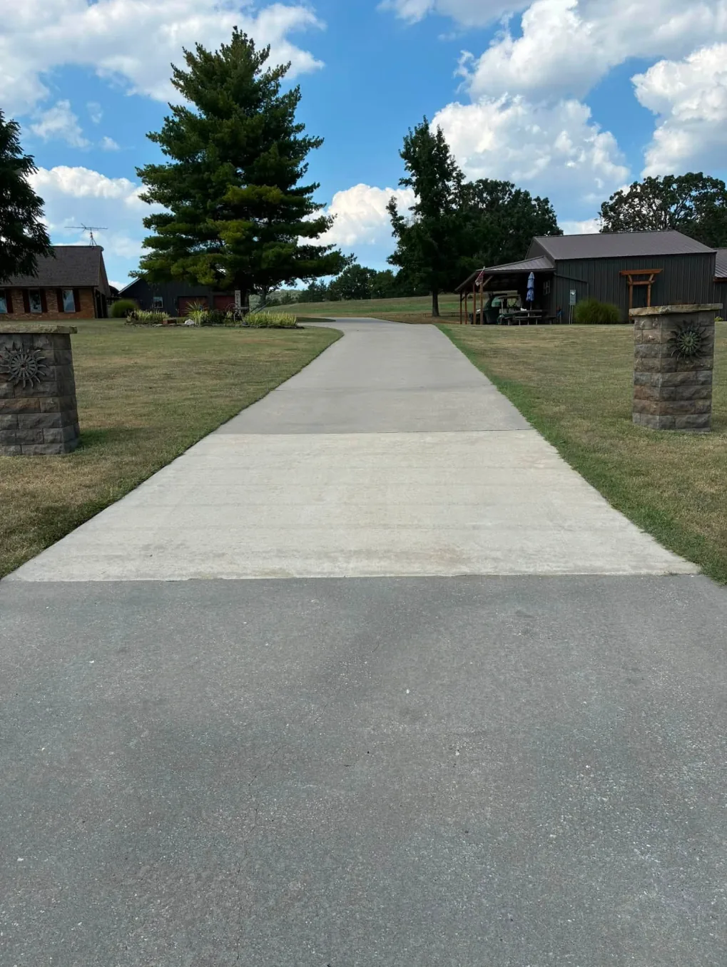 Concrete driveway running between two stone pillars toward a farm