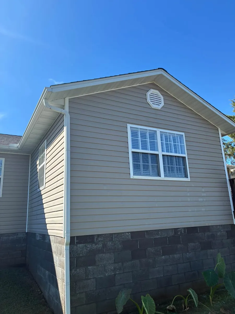 Tan sided house with a stone foundation under a blue sky