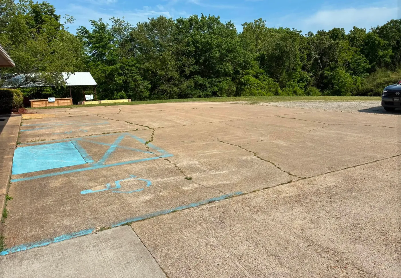Large parking area with faded blue paint and cracked, dirty concrete before washing
