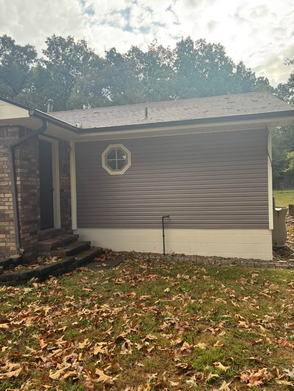 Brown vinyl sided house with an octagon window before washing