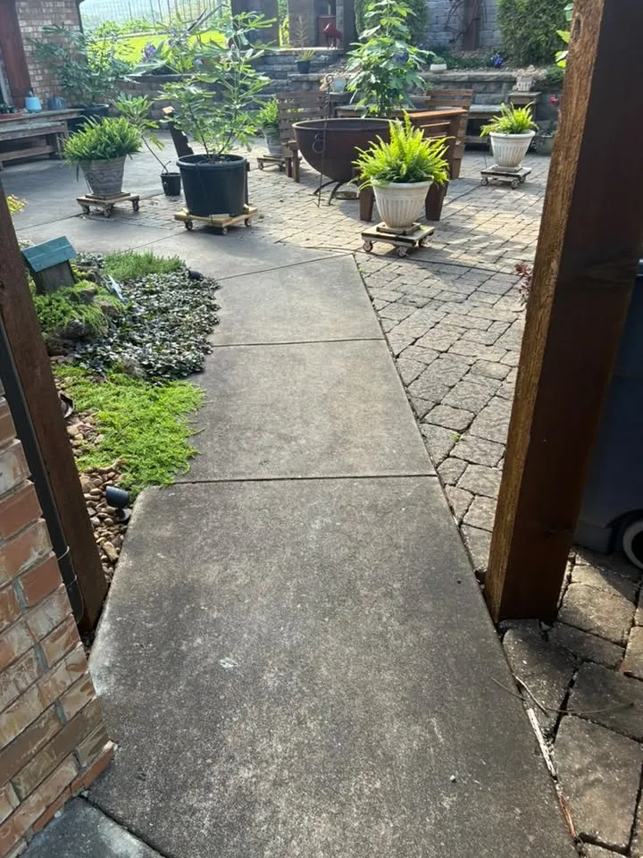Gray concrete walkway between a brick wall and a paver patio before washing