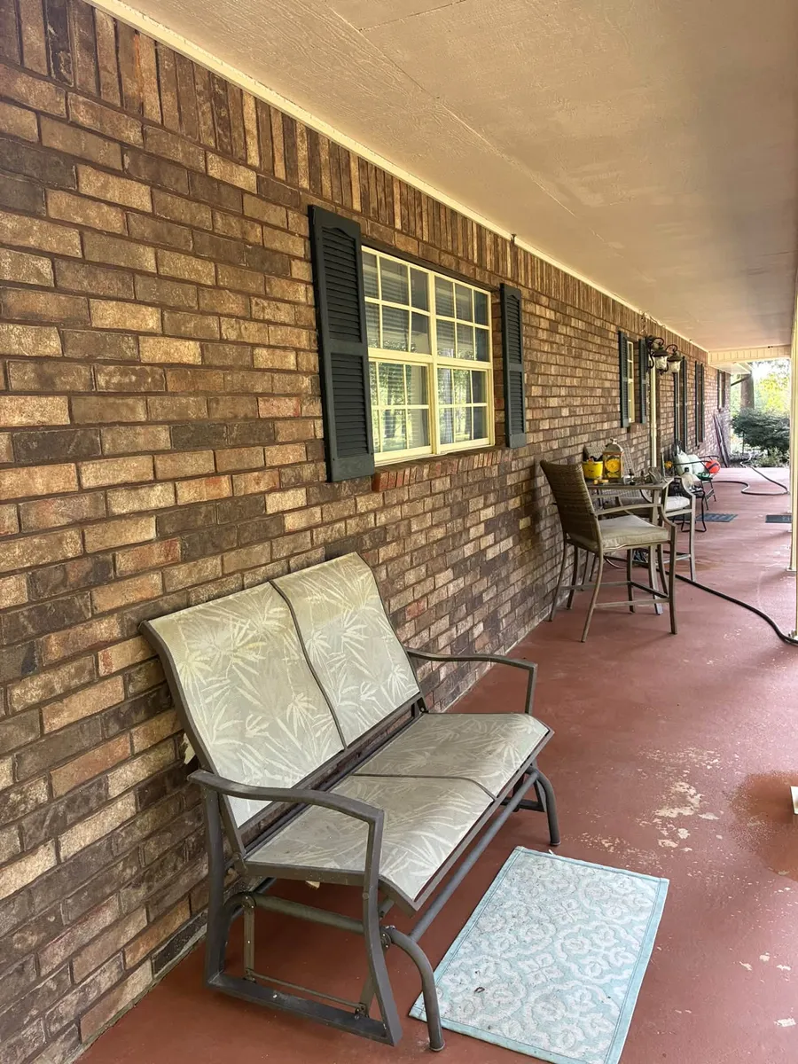Covered brick porch with a glider bench and a patterned rug