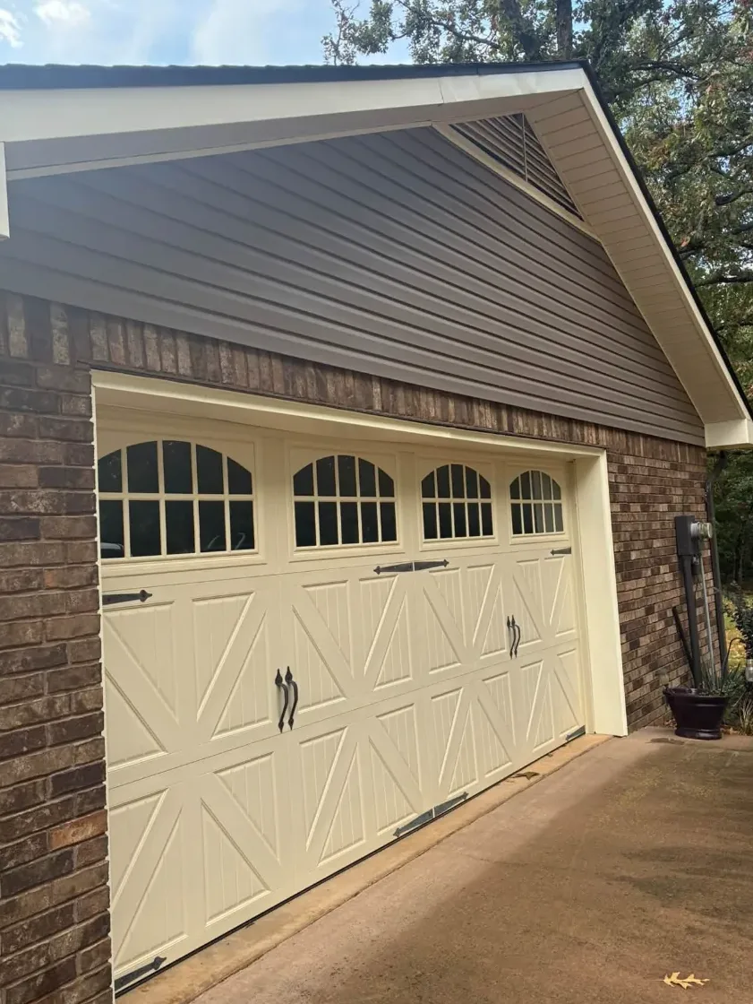 Dark, dirty concrete driveway leading to a garage with cream carriage-style doors, before washing