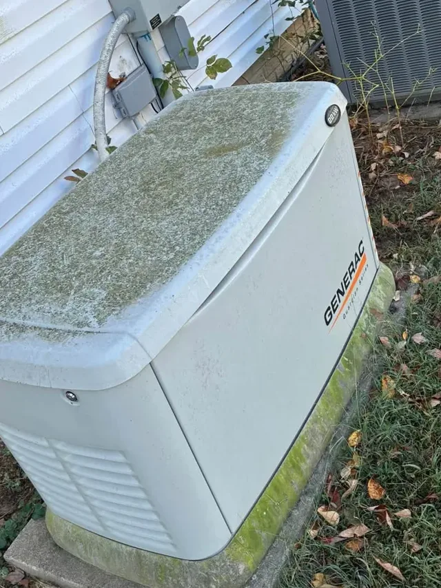 Backup generator beside white siding with green algae, before washing