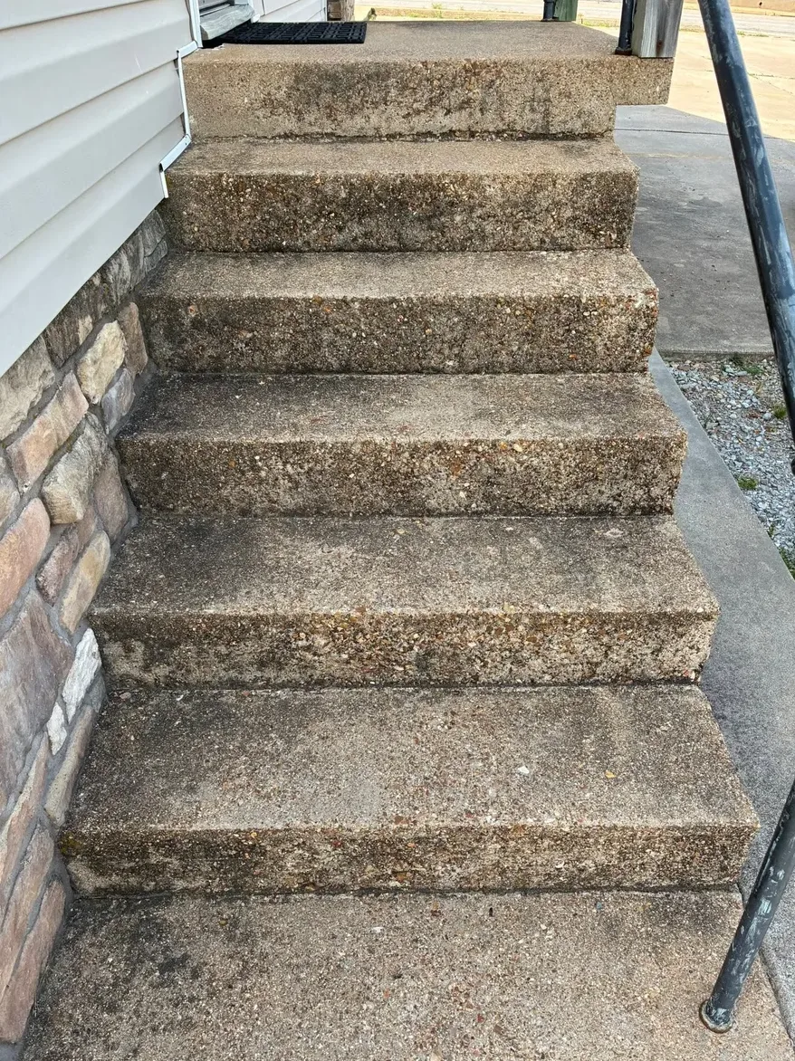 Dirty concrete steps beside a stone wall and black railing, before washing