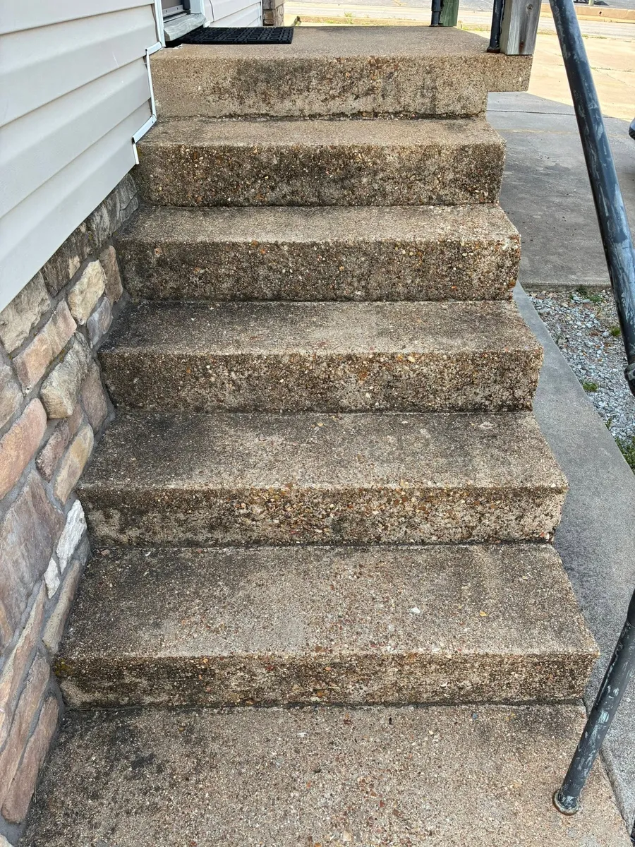 Dirty concrete steps beside a stone wall and black railing